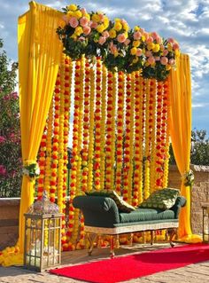 an outdoor ceremony with yellow drapes, flowers and greenery on the side wall