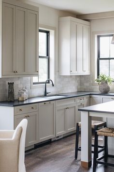 a large kitchen with white cabinets and black counter tops is pictured in this image, there are two stools at the center of the island