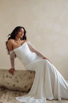 a woman in a white dress is sitting on a stone bench and posing for the camera