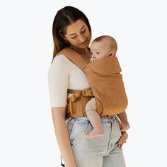 a woman is holding a baby in a brown wrap on her back while wearing jeans