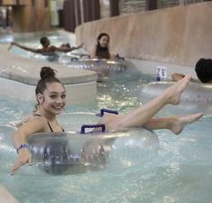 people are in an indoor swimming pool with floating rafts on the sides and one woman is smiling at the camera