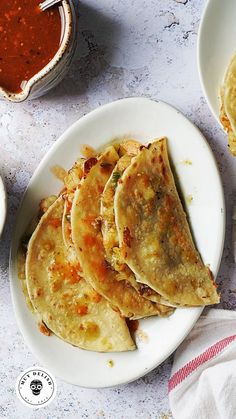 three quesadillas on a white plate next to some sauces and condiments