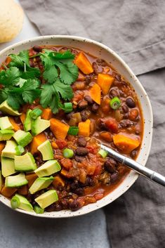 a white bowl filled with chili and avocado next to a tortilla