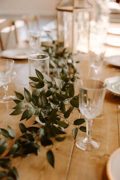 the table is set with glasses, plates and greenery