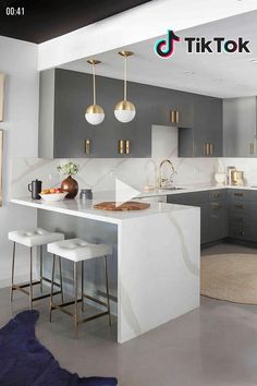 a kitchen with grey cabinets and white counter tops, gold pendant lights over the island