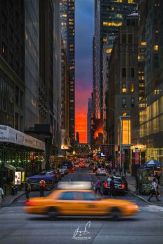 a yellow car driving down a street next to tall buildings at night with people walking on the sidewalk