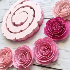 paper flowers are arranged on a white wooden surface, with pink and red ones in the center