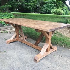 a large wooden table sitting in the middle of a park next to some grass and trees