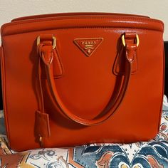 Very Good Condition Prada Handbag. Please Check Photos For Condition. Good Size Handbag For All Your Essentials. Only Callouts Are Black Ink Stain In The Interior Pocket And Some Minor Surface Cracks In One Corner Opening As Shown In Photos. Luxury Orange Handheld Bag, Luxury Handheld Orange Bag, Classic Orange Bag With Gold-tone Hardware, Orange Formal Bags With Gold-tone Hardware, Designer Orange Satchel For Shopping, Formal Orange Bags With Gold-tone Hardware, Luxury Orange Bag With Gold-tone Hardware, Designer Orange Satchel, Designer Orange Bags With Gold-tone Hardware