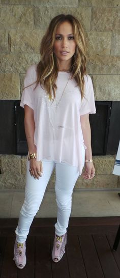 a woman standing in front of a stone wall wearing white pants and pink shoes with her hand on her hip