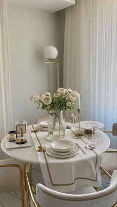 a dining room table set with white plates and gold trimmings, flowers in a vase