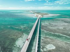 an aerial view of a highway going over the ocean and into the distance is a bridge with cars on it