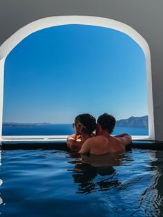 a man and woman are sitting in the pool looking out at the water from behind them