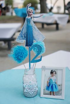 a table with a vase and photo frame on it that has a frozen princess figure in it