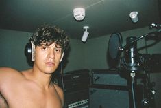 a shirtless young man wearing headphones in front of a microphone and sound equipment