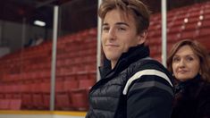 two people standing next to each other in front of an empty hockey rink with red seats