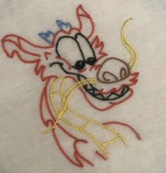 a close up of a embroidery design on a white cloth with red, yellow and blue thread