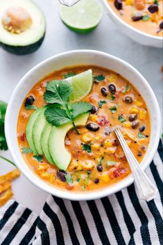 two bowls of mexican chicken soup with avocado and cilantro on the side