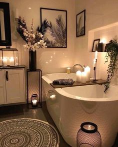 a white bath tub sitting in a bathroom next to candles and pictures on the wall