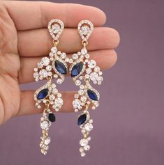 a pair of blue and white diamond earrings in someone's hand with purple background