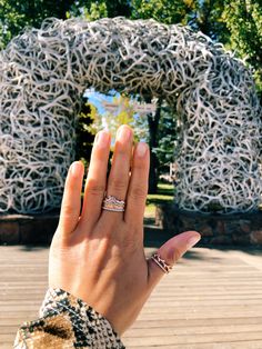 a woman's hand with two rings on her fingers in front of a sculpture