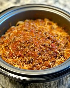 a crock pot filled with spaghetti and meat in sauce on top of a table