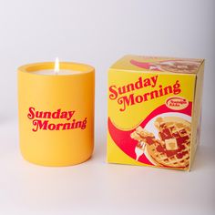 a yellow candle sitting next to a box of sunday morning waffles on a table