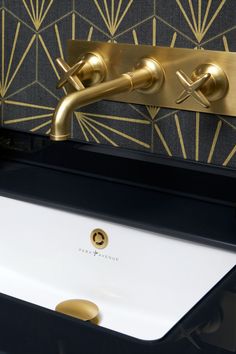 a bathroom sink with gold faucet and decorative wallpaper in the back ground