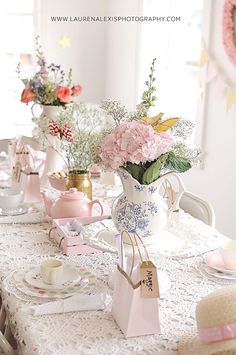 the table is set with pink flowers and teapots on it, along with other decorations