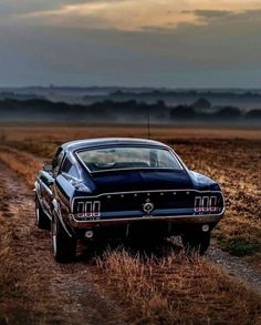 an old car is parked on the side of a dirt road in front of a field