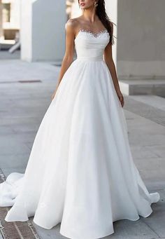 a woman in a white wedding dress standing on the sidewalk