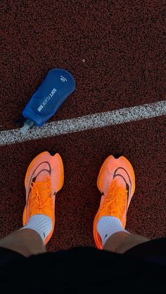 an orange tennis shoe is on the ground next to a blue trash can and a white line