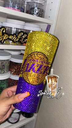 a hand is pointing at a purple and gold tumbler with the word sparkle on it