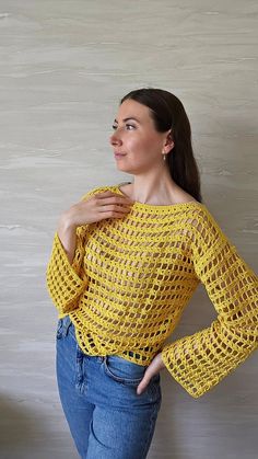 a woman standing in front of a white wall wearing a yellow crochet sweater