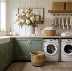 a washer and dryer in a room with green cabinets, white flowers and towels hanging on the wall