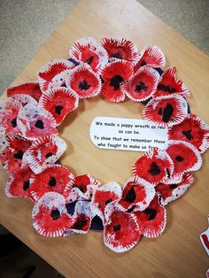 a wreath made out of red paper flowers on a table with a note that says we made a poppy wreath for remembrance