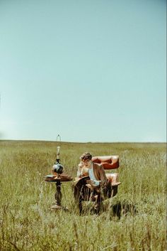 a man sitting in the middle of a field next to an old fashioned chair and table