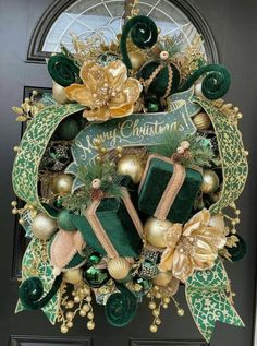 a christmas wreath with green and gold decorations on the front door, hanging from a black door