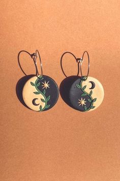 pair of black and white earrings with green leaves on them, against a brown background