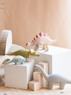 three dinosaur figurines sitting on top of white blocks in front of a pink wall