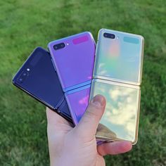 someone holding three different colored cell phones in their hands, one is purple and the other is blue