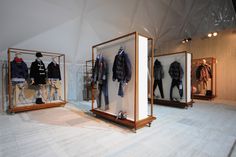 three glass cases with clothes on display in a room filled with white walls and wooden flooring