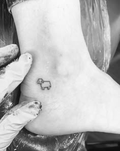 a small elephant tattoo on the foot of a woman's right foot, while she is wearing white gloves