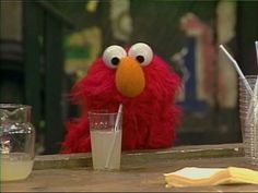 the sesame street character is sitting at a table with two drinks in front of him