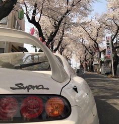 a white car parked on the side of a road next to trees with pink flowers