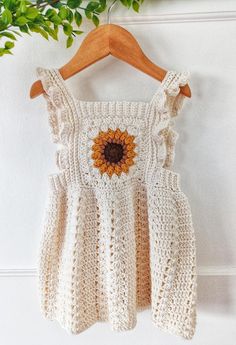 a white crocheted dress with a sunflower on the front, hanging from a wooden hanger