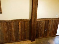 an empty room with wood paneling and two windows on the wall, in front of a door