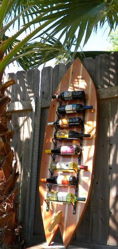 a surfboard with wine bottles on it is next to a palm tree and fence