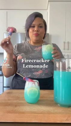 a woman is holding two glasses filled with blue and green liquid while standing in front of a counter