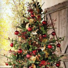 a christmas tree decorated with red and gold ornaments, berries, pine cones and greenery